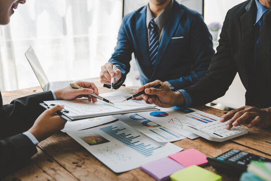 Young Colleagues Discuss Business And Analytical Price Charts Using Calculators And Laptops To Calculate Financial, Tax, Accounting, Statistics And Analytical Research Ideas.