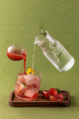 Iced strawberry drink, suspended glass and wooden tray, creative shot, green background, closeup