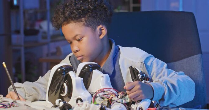 Young african american boy repairing a robotic toy at home. Smart kid assembling and testing electric circuit building and programming robot. People with futeristic technology and education concept.