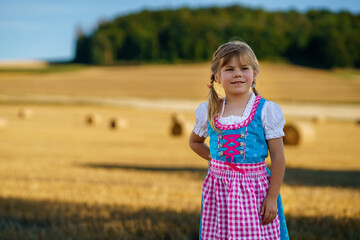 Cute little kid girl in traditional Bavarian costume in wheat field. Happy child with hay bale...