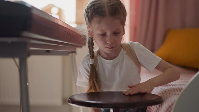 Calm little girl turns piano stool by synthesizer piano