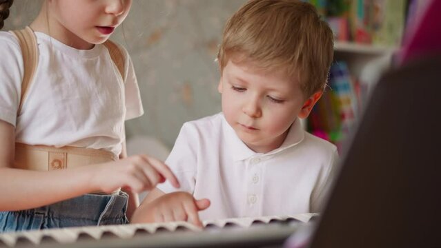 Little brother and sister press keys playing music on piano