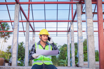 Technician talking on the phone Roof work that has not been completed in hand, holding construction drawings.