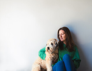 Woman and fluffy dog sitting together against a white wall.
