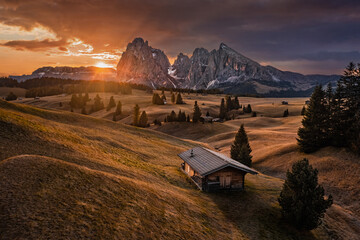 Alpe di Siusi, Italy - Golden autumn sunrise with a wooden chalet at Seiser Alm in South Tyrol province in the Dolomites mountain range with Saslonch (Sassolungo or Langkofel) mountain at background