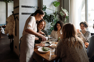 Waitress pouring wine into glasses while serving group of friends in restaurant