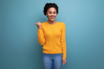 joyful young hispanic woman with black curly hair in a yellow jacket on a blue background