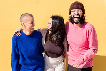 three young friends laughing and having fun together on yellow background, concept of friendship...