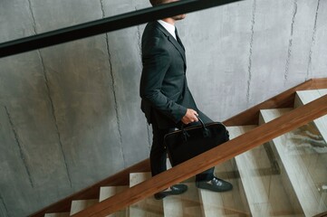 Walking up. Man in business suit and tie with case in hands is on the stairs