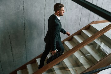 Walking up. Man in business suit and tie with case in hands is on the stairs