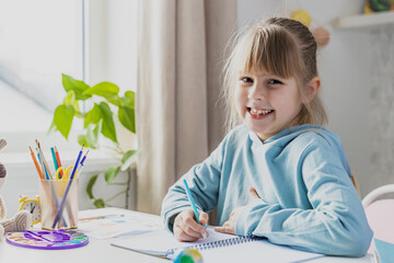 Schooler cute little girl sitting at desk in bedroom, holding pencil, doing homework, kid studying at home, writing notes. Home education, homeschooling. Child smiling, happy because of successul task