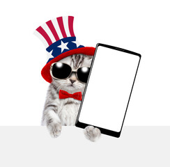 Cute kitten wearing like Uncle Sam showing big smartphone with white blank screen above empty white...