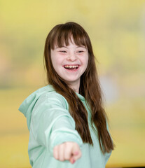 Fototapeta premium Happy young girl with Downs syndrom stands at summer park with book and points on you