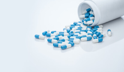 Blue-white antibiotic capsule pills spread out of plastic drug bottles. Antibiotic drug resistance. Prescription drugs. Healthcare and medicine. Pharmaceutical industry. Pharmacy product. Medication.