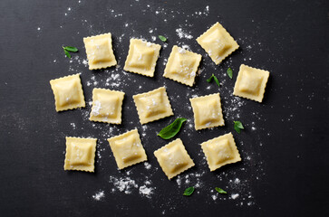 Raw Ravioli with Flour and Basil on Dark Background