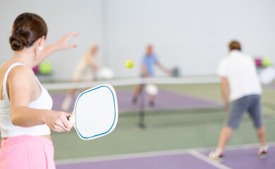 White paddle-shaped racquet for pickleball in hand of young female player swinging to hit ball...