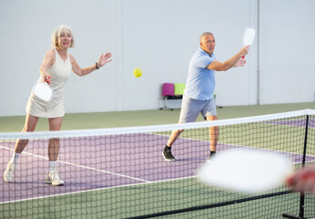 Obraz premium Athletic seniors playing pickleball on the court indoors