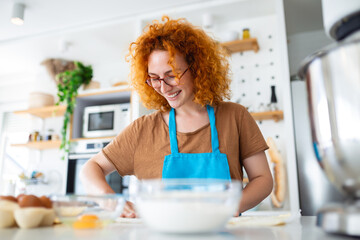 Happy attractive young adult woman housewife baker wear apron holding pin rolling dough on kitchen table baking pastry concept cooking cake biscuit doing bakery making homemade pizza at home