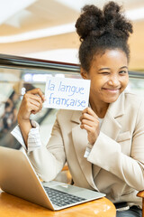 Happy smiling African woman showing French vocab flash card, education concept of language of...