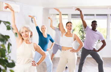 Fototapeta premium Portrait of elderly woman enjoying active dancing during training with mixed age group in dance studio