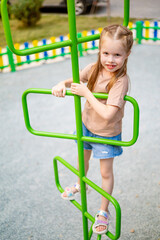 a child girl on a children's multi-colored playground in the courtyard of a multi-storey house in the summer has fun playing and climbing high up the stairs, summer holidays