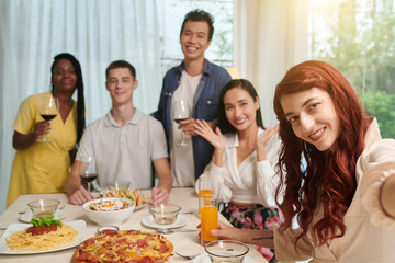 Fototapeta na wymiar Positive red hair young woman photographing with friends at dinner party