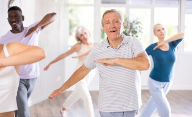 Enthusiastic elderly man practicing modern vigorous dance movements in group dance class with...