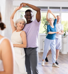 Cheerful senior woman practicing passionate samba with interested african american man in dance...