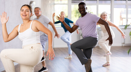 Fototapeta premium Young woman coach rehearsing with group of multinational sports aged people hip hop dance in dance hall