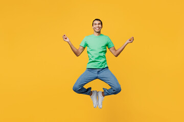 Fototapeta na wymiar Full body young man of African American ethnicity he wears casual clothes green t-shirt hat jump high spread hands in yoga om aum gesture relax meditate, calm down isolated on plain yellow background.