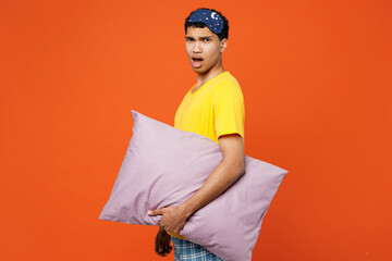 Side view young annoyed disturbed tired man he wearing pyjamas jam sleep eye mask rest relax at home look camera isolated on plain orange wall background studio portrait. Bad mood night nap concept.