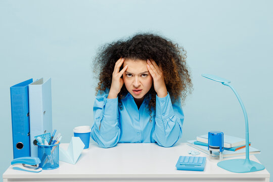 Young tired stressed troubled employee business woman wear casual shirt sit work at white office desk look camera hold head rub temples isolated on plain pastel light blue background studio portrait.