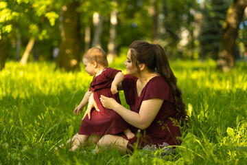 Fototapeta premium Sun-kissed and joyful: A mother's love shines as brightly as the sun as she shares a moment of joy with her one-year-old daughter in the park. Concept: Happy Motherhood