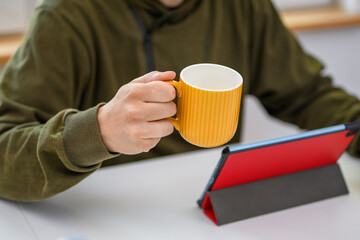 Mężczyzna przeglądający poranne wiadomości na komputerze popijający kawę z kubka
