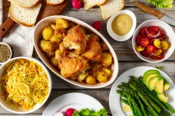 Home dinner table with healthy food. Set of various food from baked new potatoes with chicken thighs, vegetables and salads on wooden table top view