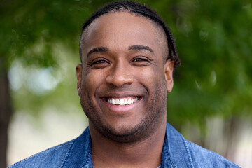 Close-up portrait of a popular smiling black blogger in jeans on a green blurry background. Smiling successful African-American blogger, influencer
