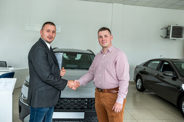 man buys an expensive car representative of car dealership shakes his hand as sign of agreement