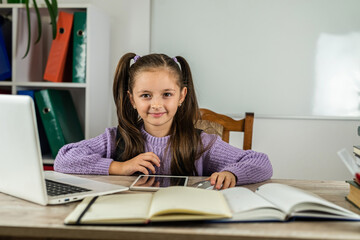 smiling little girl is watching a video lesson on the computer.