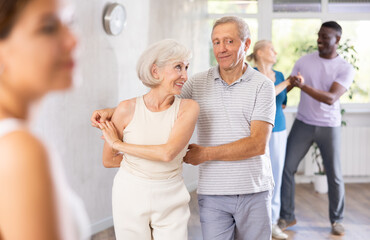 Happy smiling elderly woman enjoying impassioned merengue with male partner in latin dance class. Social dancing concept