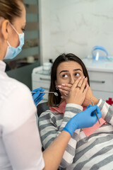 Young female patient covering her mouth with hands at the dentist's appointment