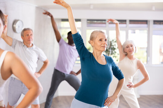 Aged woman takes part in dance class with diverse group of individuals who are enthusiastic about outdoor activities. This multinational group is actively involved in dance lesson and enjoying it.