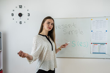 Young female teacher stand near whiteboard and explain english language rules or grammar