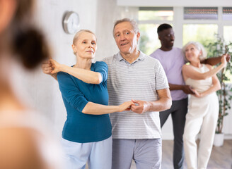 Mature man dances in couple with senior lady and learns Latin dance with other students. Physical activity, good bodily shape