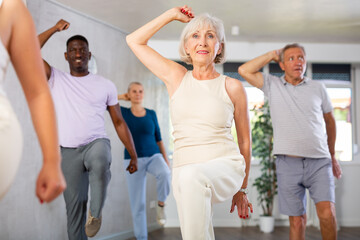 Fototapeta premium Positive emotional senior woman learning to dance krump with group in modern choreographic studio