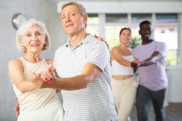 Dynamic young and mature attendees of dancing courses training poses of Waltz in dance hall