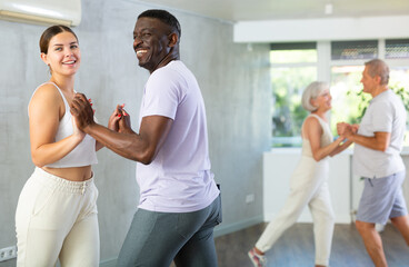 Happy attractive young girl enjoying impassioned merengue with experienced African American partner...