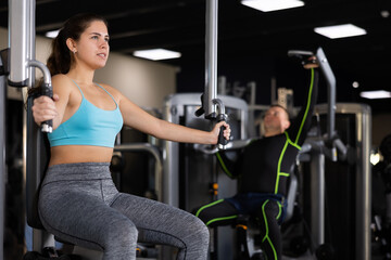 Fototapeta na wymiar Concentrated young girl leading healthy active lifestyle doing strength training in gym, performing butterfly exercise for chest muscles in pec deck machine ..