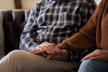 Senior man emotionally supporting and comforting his senior wife while holding her hands.