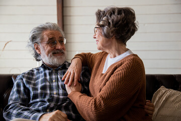 Dreamy elderly loving middle aged retired couple looking at each other, planning a common future or reminiscing about memories while enjoying a quiet moment of relaxation together on a cozy sofa in