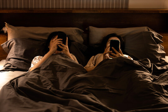 Asian female with nomophobia(No mobile phone phobia)lying on bed using smartphone in bedroom at night or symptom of Revenge Bedtime Procrastination,disease of Insomnia,mobile syndrome,social addiction